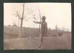 Photograph of an unidentified Miami Military Institute cadet on a hillside, pointing a gun, 1904