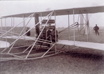 Orville Wright and a passenger seated in the Flyer
